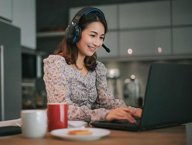 A woman sits at desk in front of computer working from home