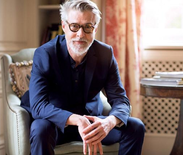 Man with gray hair and glasses posing on a chair for the camera