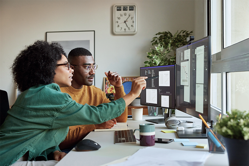 A man and woman sit at a desk looking at computer screens