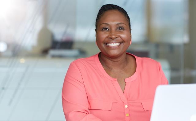 A woman sits at a desk with computer, smiling